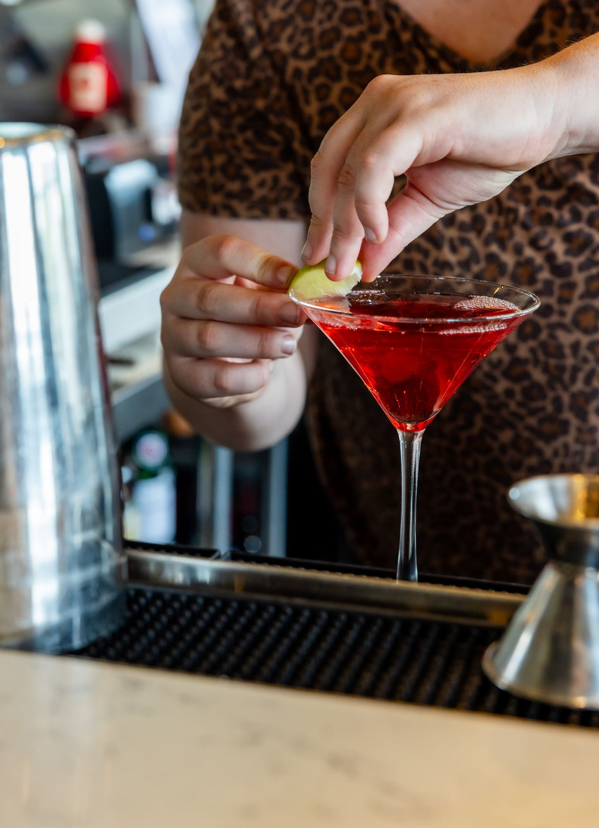 A bartender adding a lime to a red martini