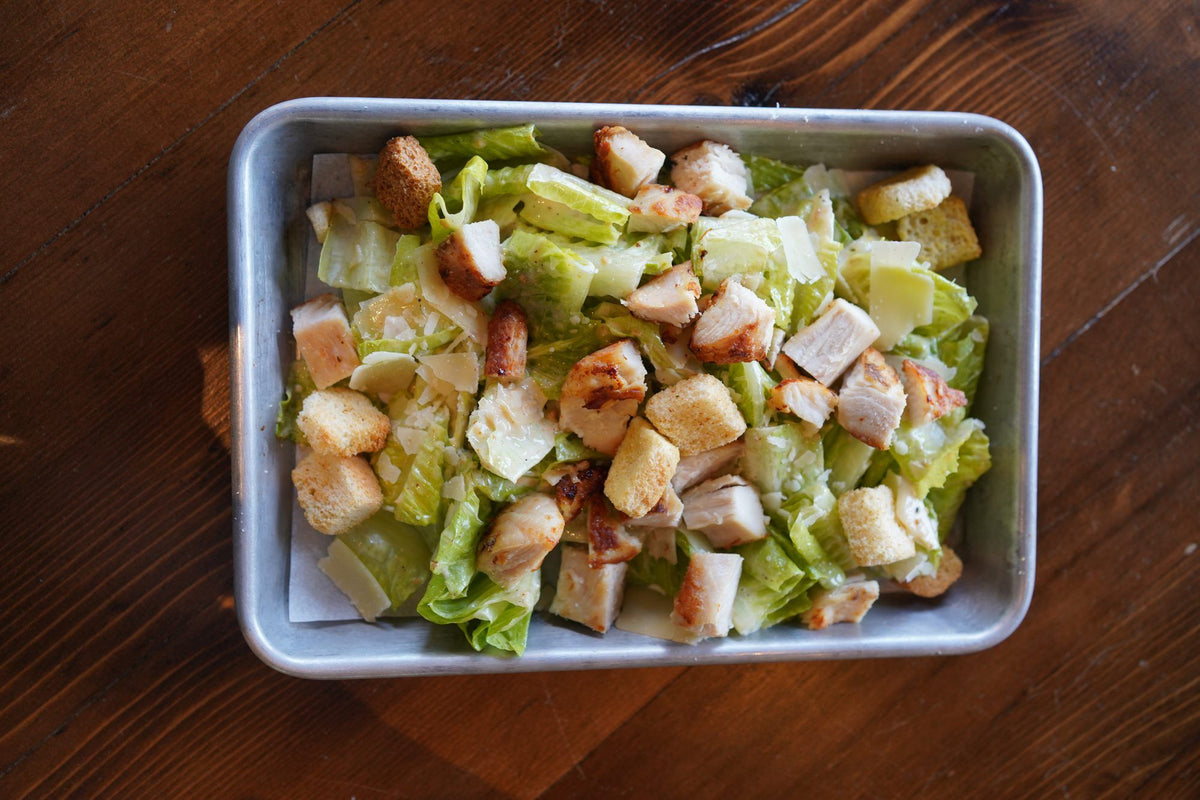 A Caesar salad with grilled chicken, croutons, and shaved Parmesan