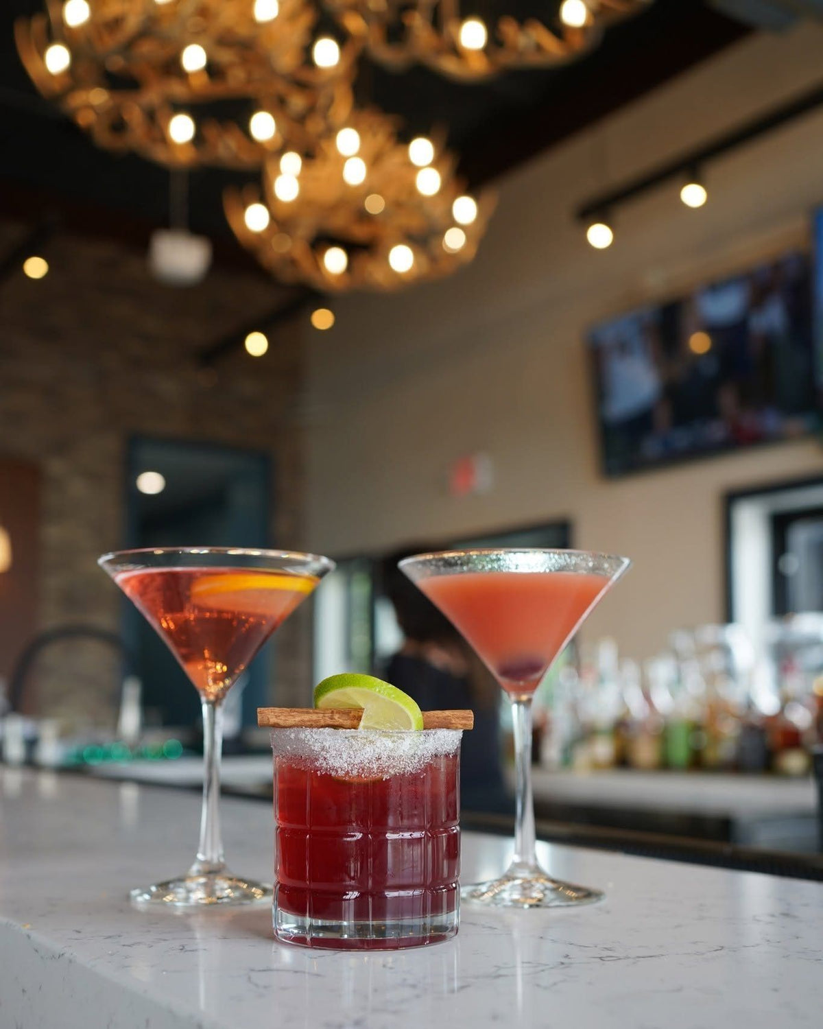 Three house cocktails on the bar under glowing antler chandeliers