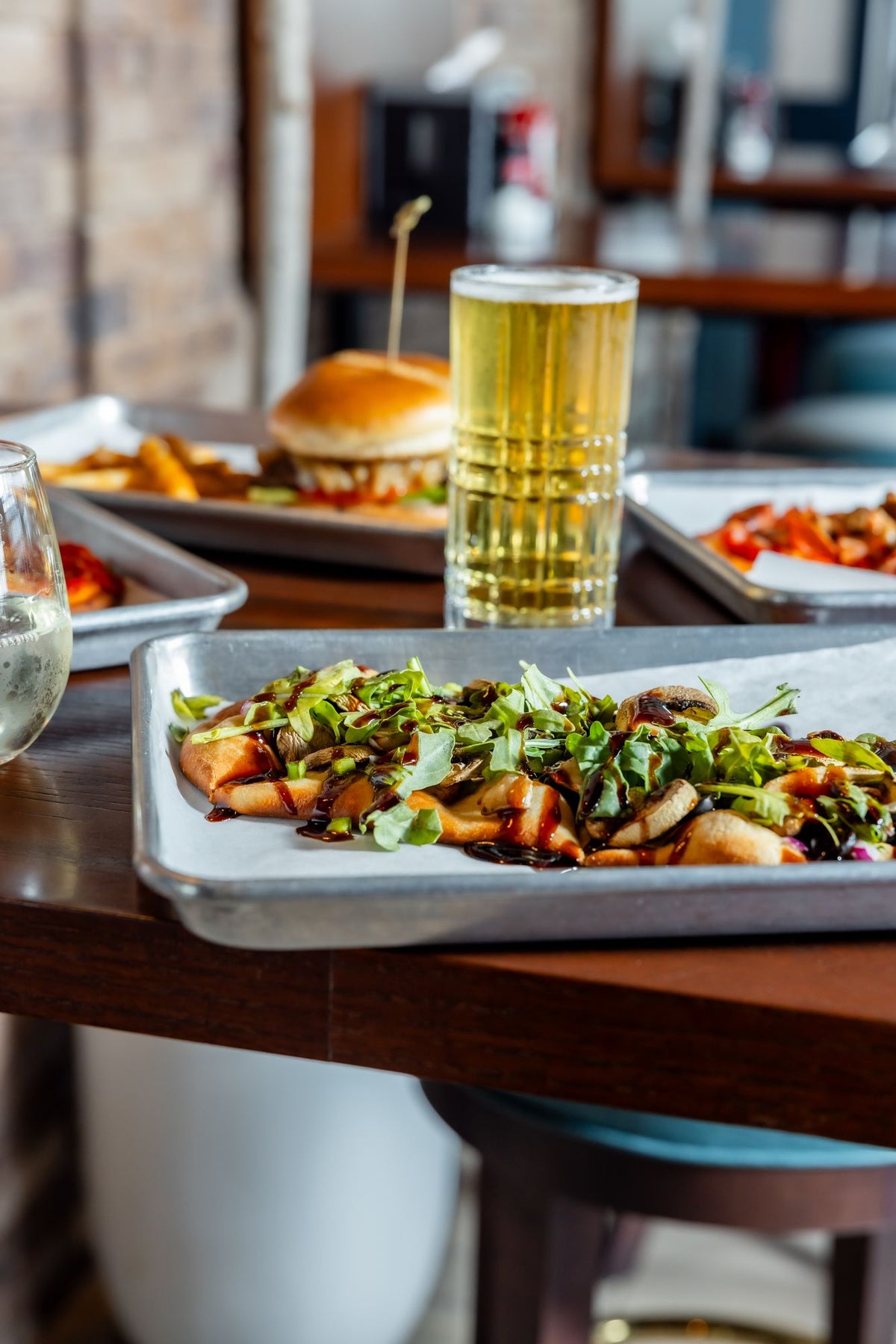 A flatbread pizza on a tray, with a beer and a burger behind it