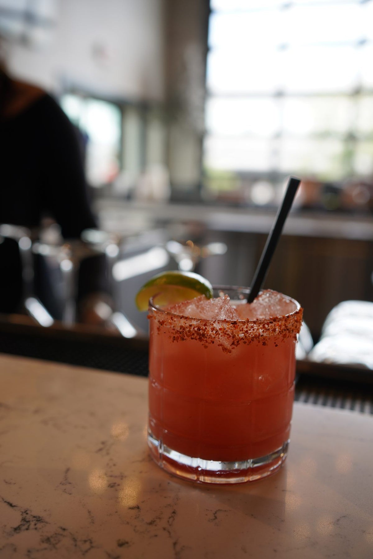 A margarita with a Tajín rim and a lime wedge on the bar